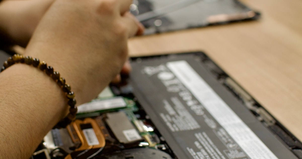 Technicien retirant la batterie d'un ordinateur portable ouvert sur un plan de travail